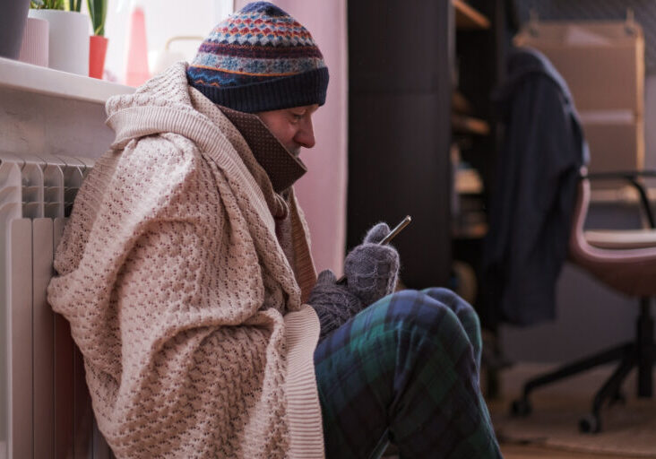 Man feeling cold at home having problems with home heating sitting with phone. No money for paying service